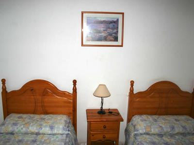 Zwei Einzelbetten mit Holzrahmen, Nachttisch dazwischen, Lampe und Wandbild darüber.