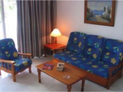Kleines Wohnzimmer mit blau gemustertem Sofa und Sessel, Holzmöbeln und warmem Licht.