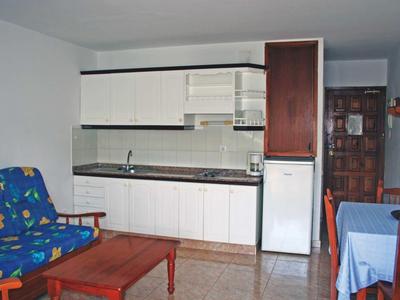 Kleine Küche mit weißen Schränken, Holztisch, blauer Tischdecke und blauem Sofa mit Blumenmuster.