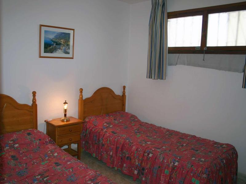 Kleines Schlafzimmer mit zwei Einzelbetten, roter Bettwäsche, Nachttisch und Fenster mit Vorhängen.