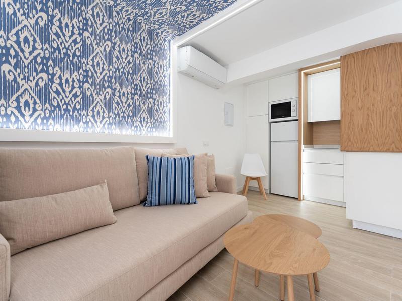 Nowoczesny salon z beżową sofą, niebieską zasłoną w wzory i drewnianymi meblami.