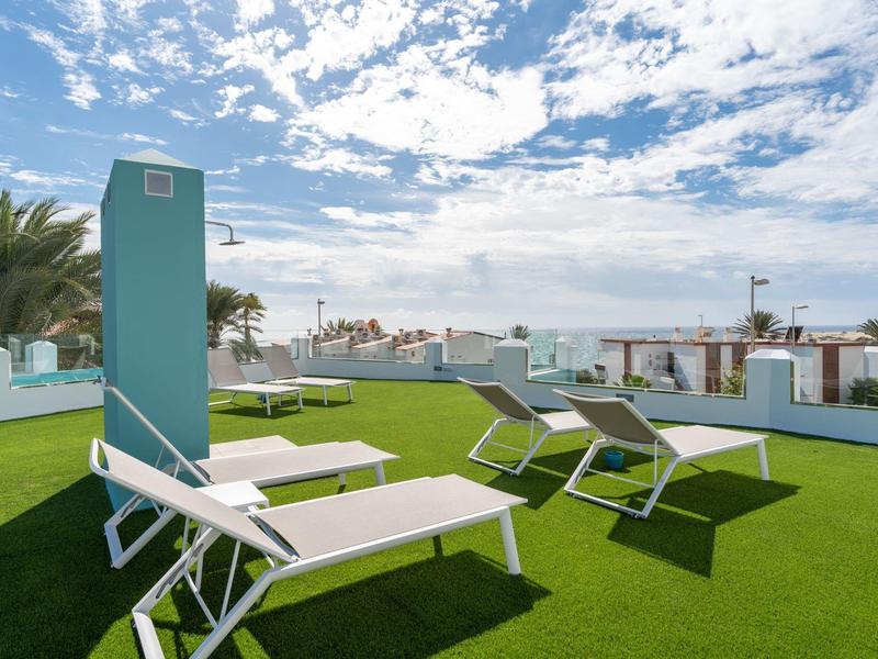 Taras słoneczny z leżakami i zieloną trawą pod niebieskim niebem.