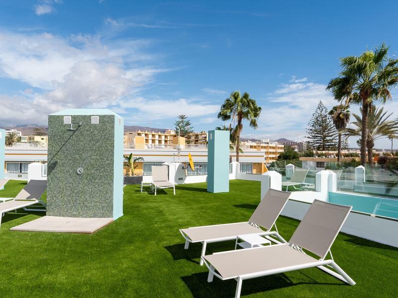 Taras słoneczny z leżakami, prysznicami i palmami pod niebieskim niebem.