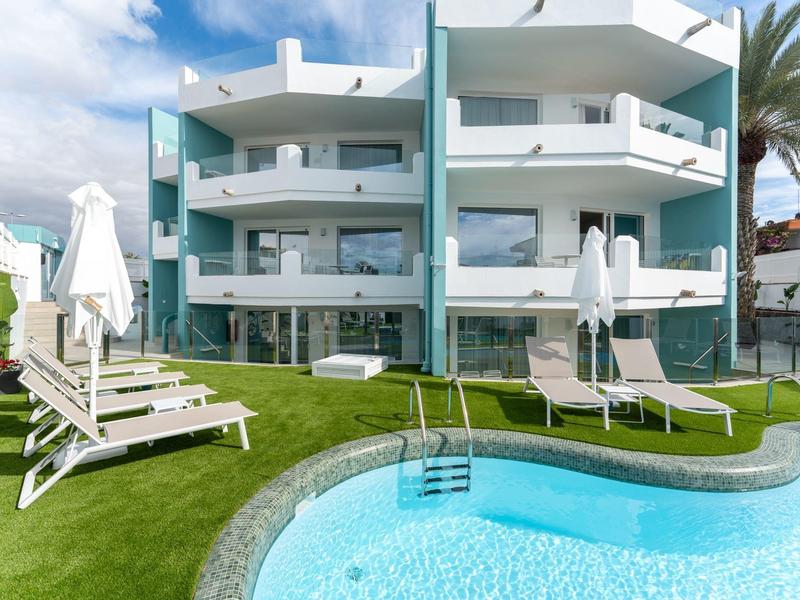 Nowoczesny hotel z basenem, leżakami i zielonym trawnikiem pod niebieskim niebem.