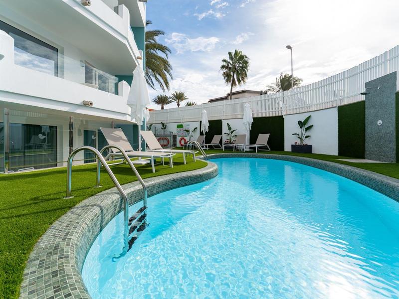 Nowoczesny basen hotelowy z tropikalnymi palmami i leżakami w słoneczny dzień.