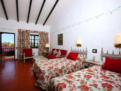 Zimmer mit zwei Betten, rot-weiß geblümter Bettwäsche, roten Stühlen und Holzbalkendecke.