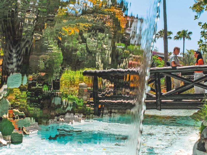 Tętniący życiem basen hotelowy z wodospadami i bujną tropikalną roślinnością na zewnątrz.