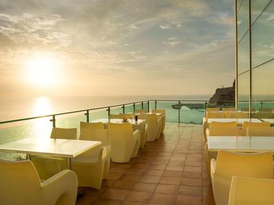 Zonsondergang vanaf buitenterras met gele stoelen en glazen reling bij de zee.