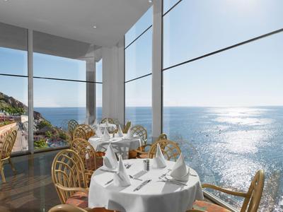 Restaurant met ronde tafels bij grote ramen met uitzicht op de zonovergoten zee