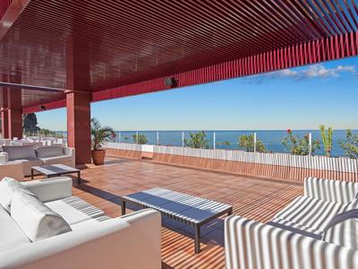 Ruim terras met banken en uitzicht op zee onder een rood plafond.