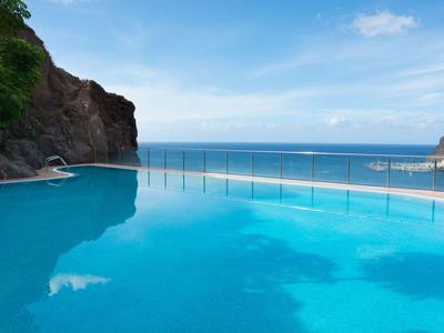 Basen infinity z widokiem na morze i skaliste wzgórze pod niebieskim niebem.