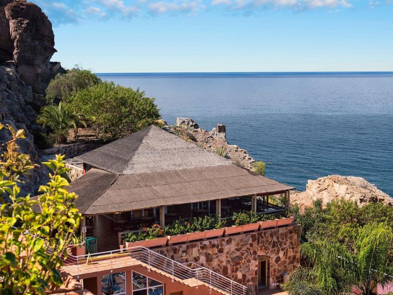 Steenhuis met rieten dak met uitzicht op rustige zee en rotsachtige kliffen