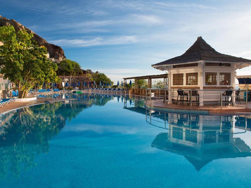 Buitenzwembad met ligstoelen en een paviljoen onder een heldere hemel.