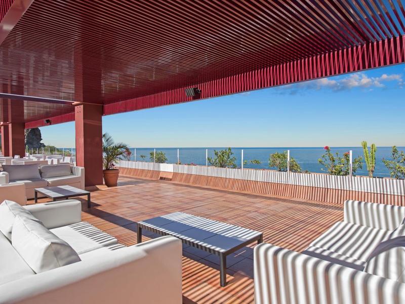 Ruim terras met banken en uitzicht op zee onder een rood plafond.