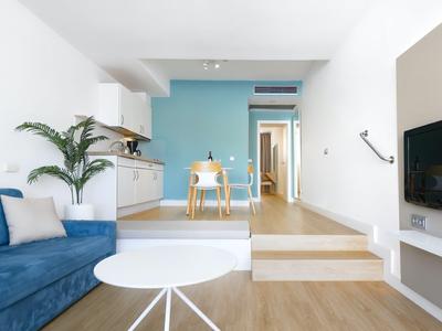 Modern living room with kitchenette, blue sofa, and white table.