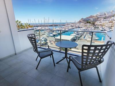 Balcony with table and two chairs overlooking a marina and white buildings.