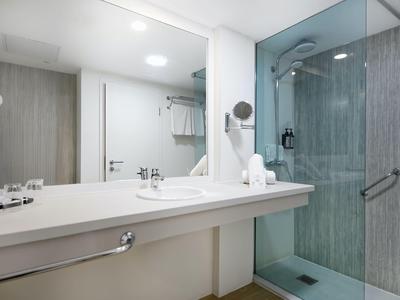 Modern hotel bathroom with large shower, sink, and white walls.