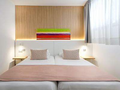 Modern hotel room with two single beds, light wood, and colorful wall decoration.