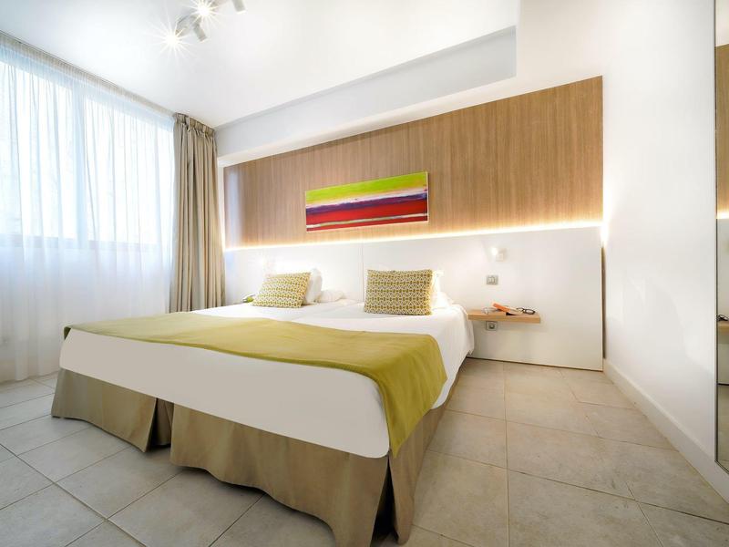 Chambre d'hôtel moderne avec grand lit, panneau mural en bois et lumière vive de la fenêtre.