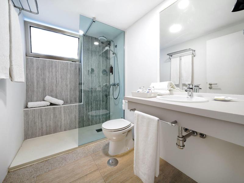 Salle de bain moderne avec douche en verre, lavabo blanc, toilettes et sol en bois.