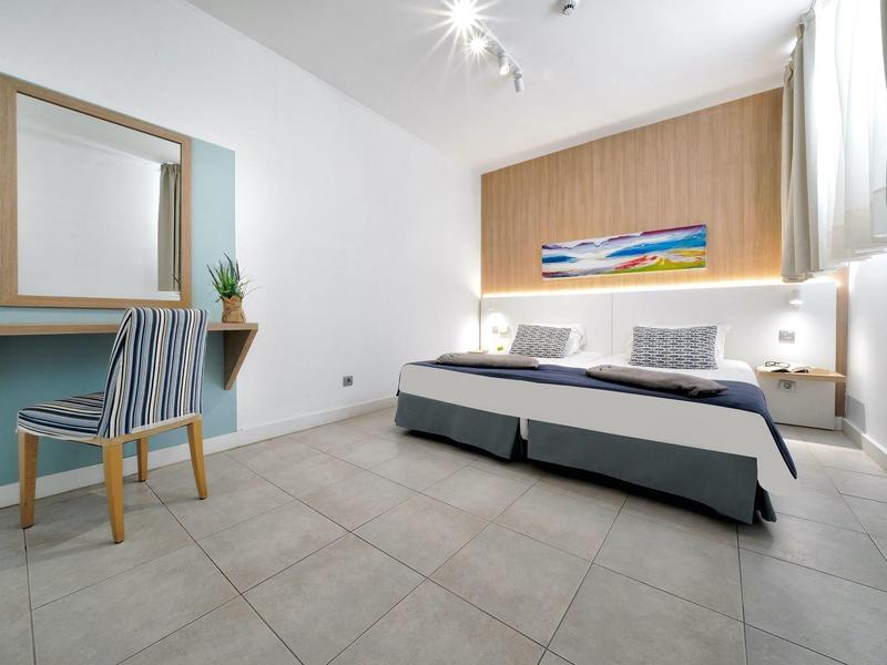 Chambre d'hôtel moderne avec lits jumeaux, tête de lit en bois, bureau et grand miroir.