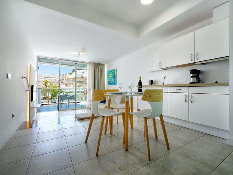 Cuisine lumineuse avec armoires blanches, table à manger et chaises donnant sur un balcon avec vue sur la mer.