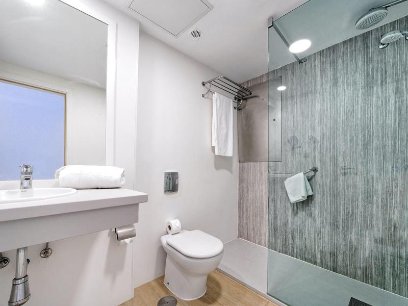 Salle de bain moderne avec douche en verre, lavabo blanc, toilettes et porte-serviettes dans une chambre d'hôtel.