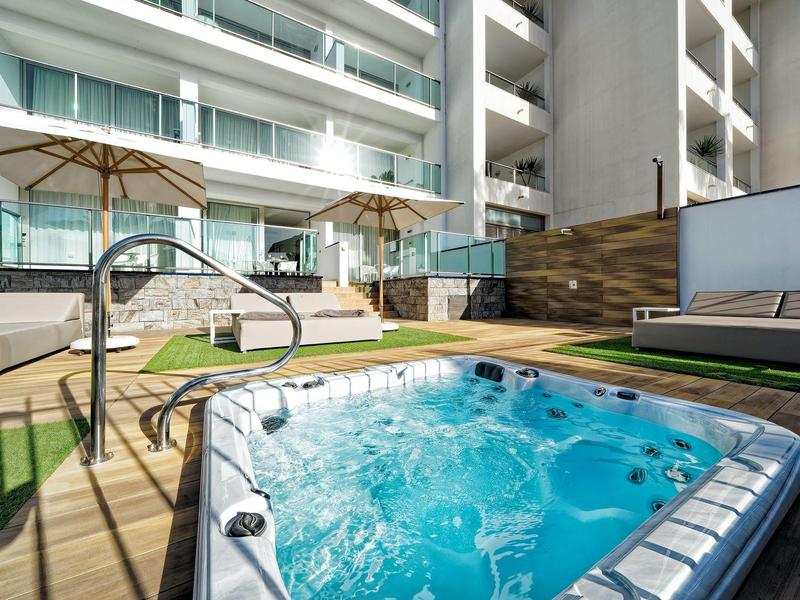 Jacuzzi extérieur avec eau bouillonnante sur une terrasse d'hôtel avec chaises longues et parasols.