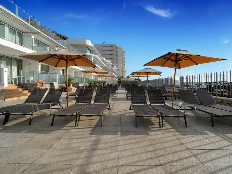 Chaises longues vides et parasols disposés sur une terrasse d'hôtel sous un ciel bleu clair.