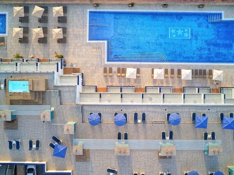 Vue aérienne d'une piscine d'hôtel avec transats, parasols et jacuzzi.