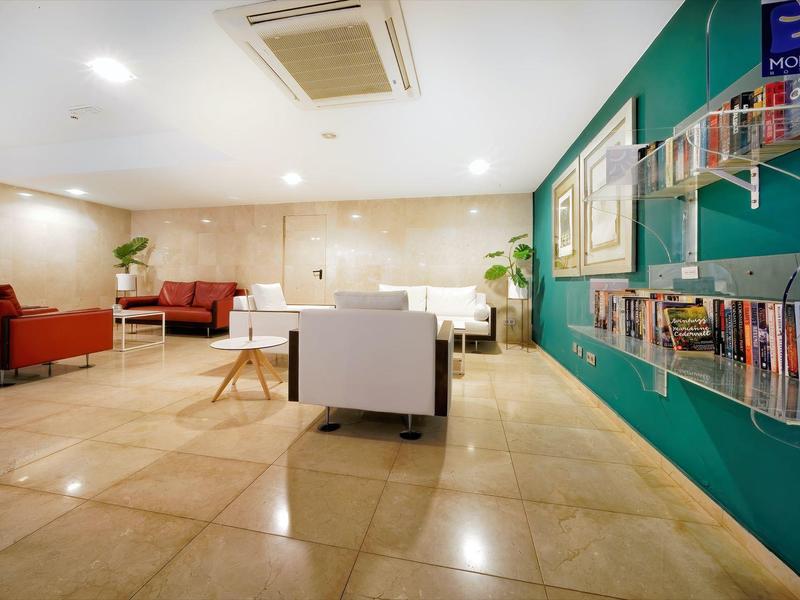 Hall d'hôtel moderne avec espaces assis, mur accent vert, magazines et sol beige.