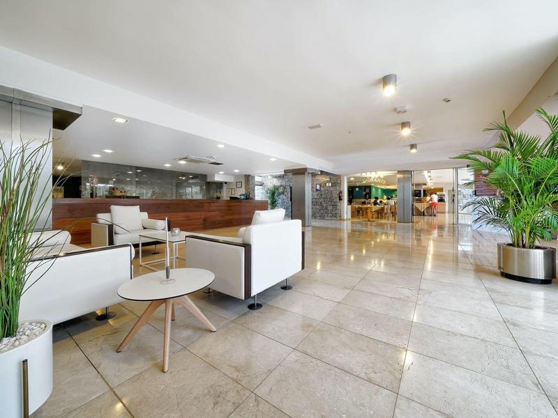 Hall d'hôtel spacieux avec canapés blancs, plantes et sol en marbre sous un éclairage lumineux.