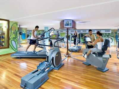 Salle de sport moderne avec sol en bois et personnes utilisant des machines d'exercice.