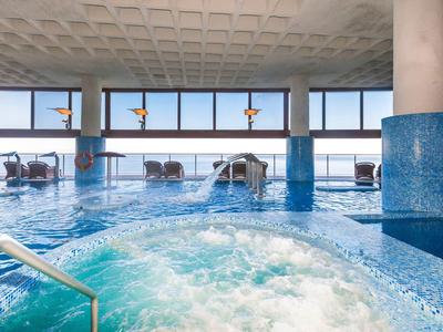 Innenpool mit sprudelndem Whirlpool, blauen Wänden, großen Fenstern und moderner Beleuchtung.