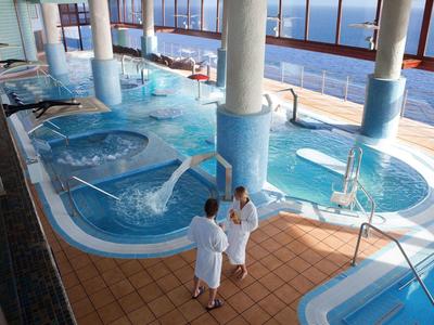 Innenbereich mit Whirlpools, blauen Wasserbecken und Menschen in weißen Bademänteln.