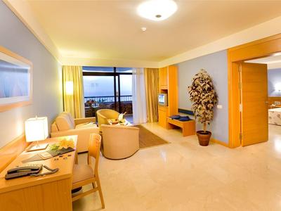 Helles Wohnzimmer mit beigem Sofa, Holzmöbeln, großem Fenster und Stadtblick bei Dämmerung.