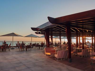Terrasse d'hôtel avec espaces assis et parasols au coucher du soleil au bord de la mer.