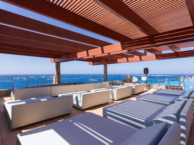 Offener Dachbereich mit weißen Sofas, Holzdach und Blick aufs blaue Meer im Hintergrund.