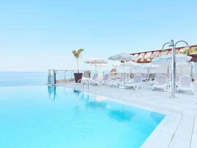 Infinity-Pool mit klarblauem Wasser und weißen Liegestühlen unter Sonnenschirmen bei klarem Himmel.