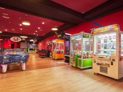 Salle de jeux colorée avec table d'air hockey et diverses machines à jeux sur sol en bois clair.