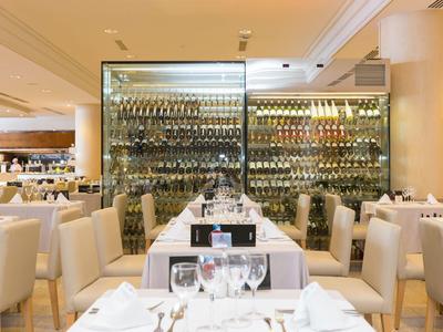 Elegantes Restaurant mit weißen Stühlen, gedeckten Tischen und großer Weinwand im Hintergrund.