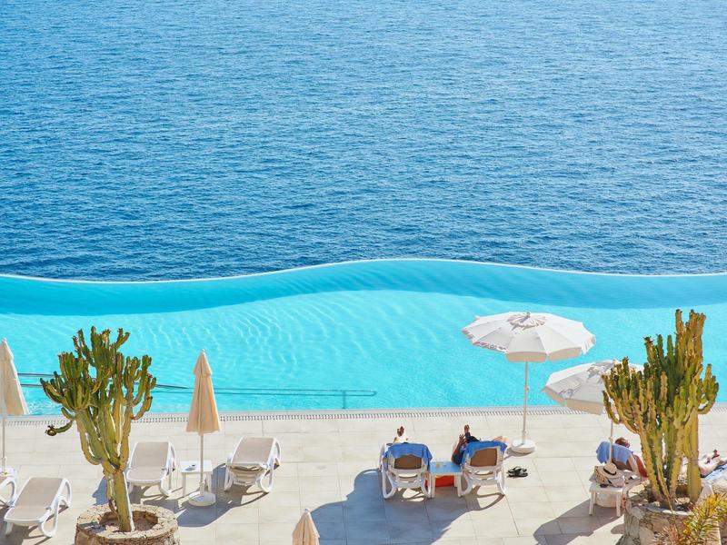 Meerblick mit hellem Sandstrand, Liegestühlen, Sonnenschirmen und vereinzelten Kakteen.