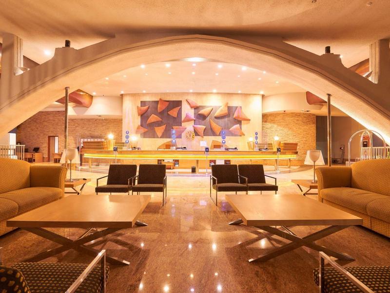 Helles, modernes Hotellobby mit Sitzgruppen, beleuchtetem Tresen und kunstvoller Architektur.