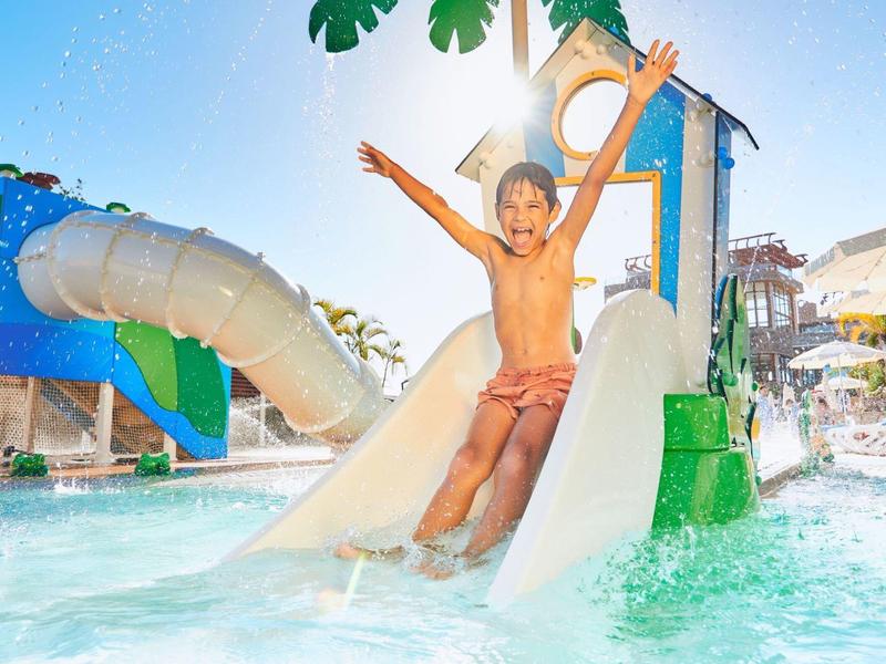 Junge rutscht fröhlich auf einer weißen Wasserrutsche in einem sonnigen Wasserpark.