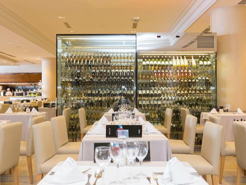 Elegantes Restaurant mit weißen Stühlen, gedeckten Tischen und großer Weinwand im Hintergrund.