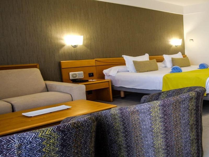 Modernes Hotelzimmer mit zwei Doppelbetten, Sofa, Sessel und sanfter Beleuchtung.