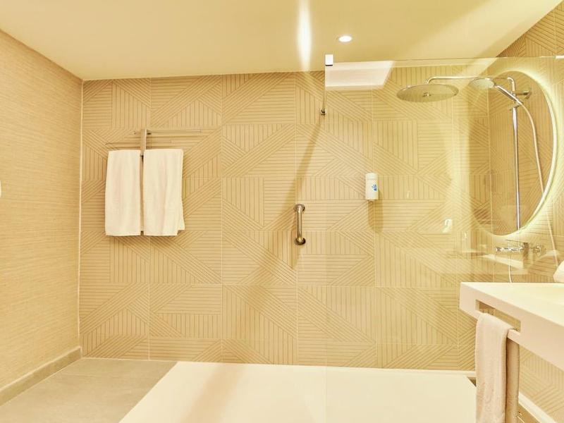 Helles Badezimmer mit Glasdusche, weißem Waschbecken, Handtüchern und Bademantel an der Wand.