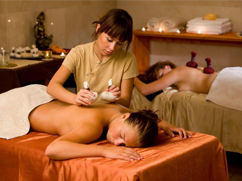 Eine Frau massiert den Rücken einer liegenden Person in einem warm beleuchteten Massageraum.