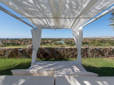 Coin salon ensoleillé sous un auvent blanc avec vue sur un paysage vert.