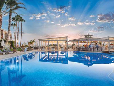 Grande piscine d'hôtel avec palmiers et espaces lounge confortables au coucher du soleil.
